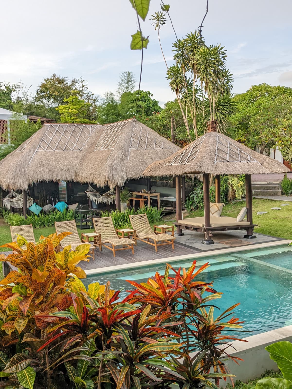Pool, thatched bales and sun loungers in the tropical garden